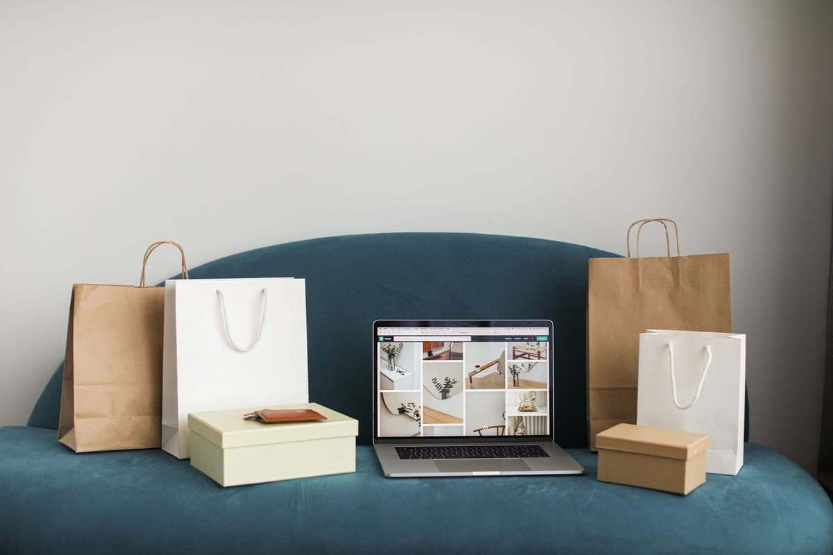 Un laptop cu un magazin online deschis, între pungi și cutii, pe o canapea